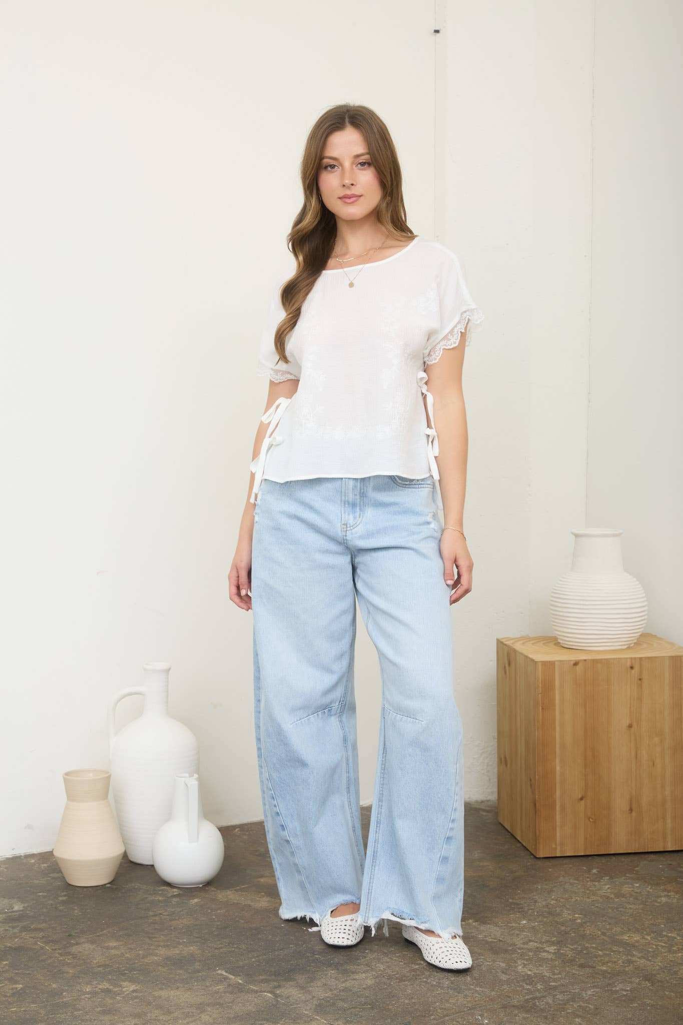 Woman wearing a white top and light blue jeans standing in a room with decorative vases.