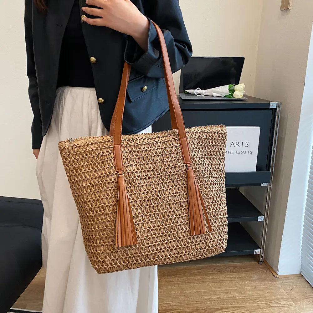 Person holding a woven handbag with brown straps in an indoor setting