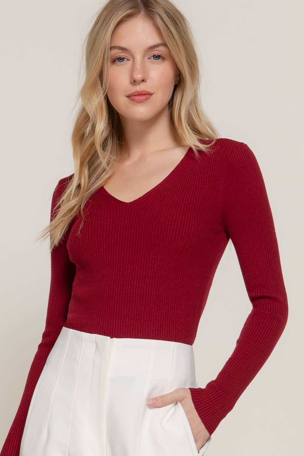 Woman wearing a red sweater and white pants against a plain background