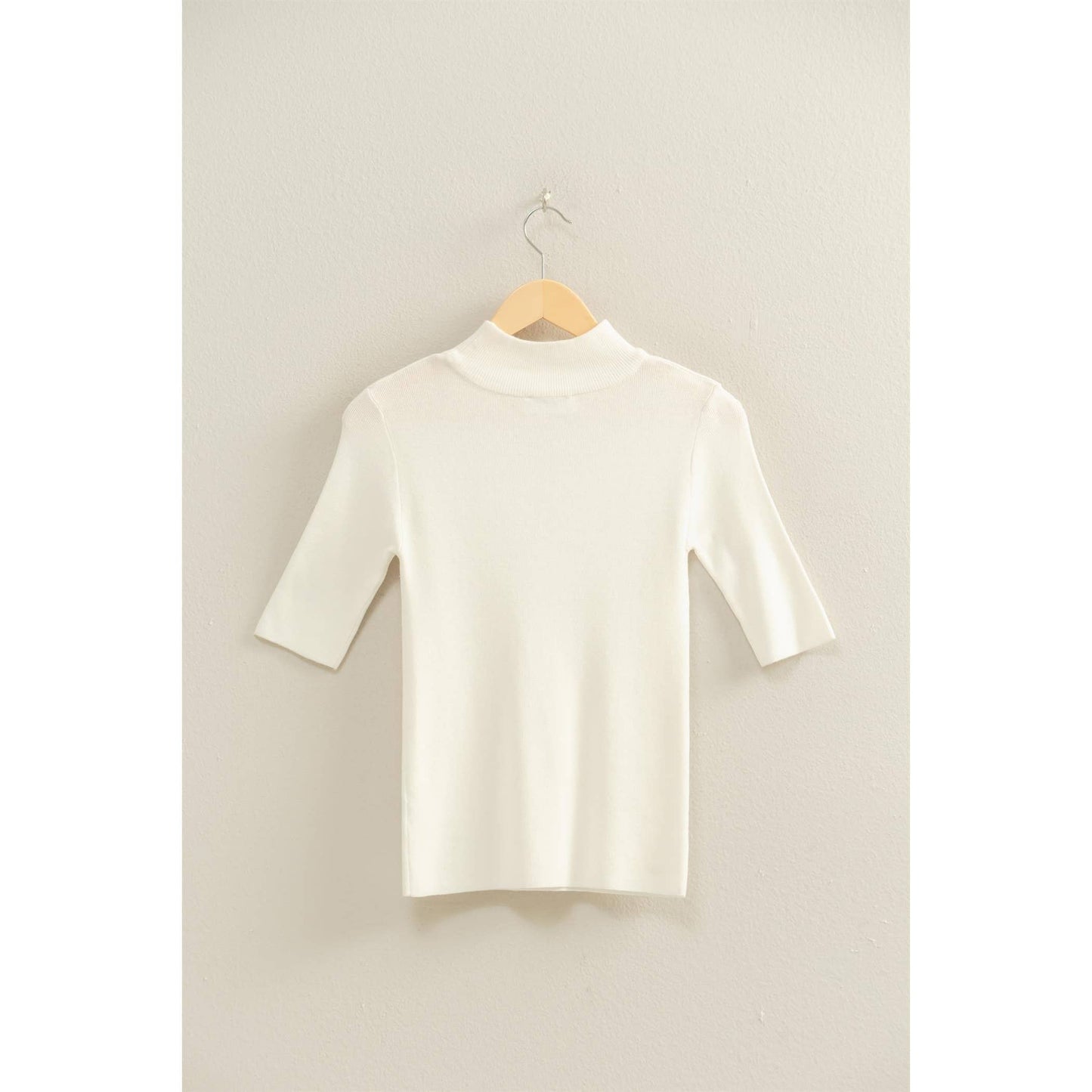 White turtleneck sweater on a hanger against a light gray background