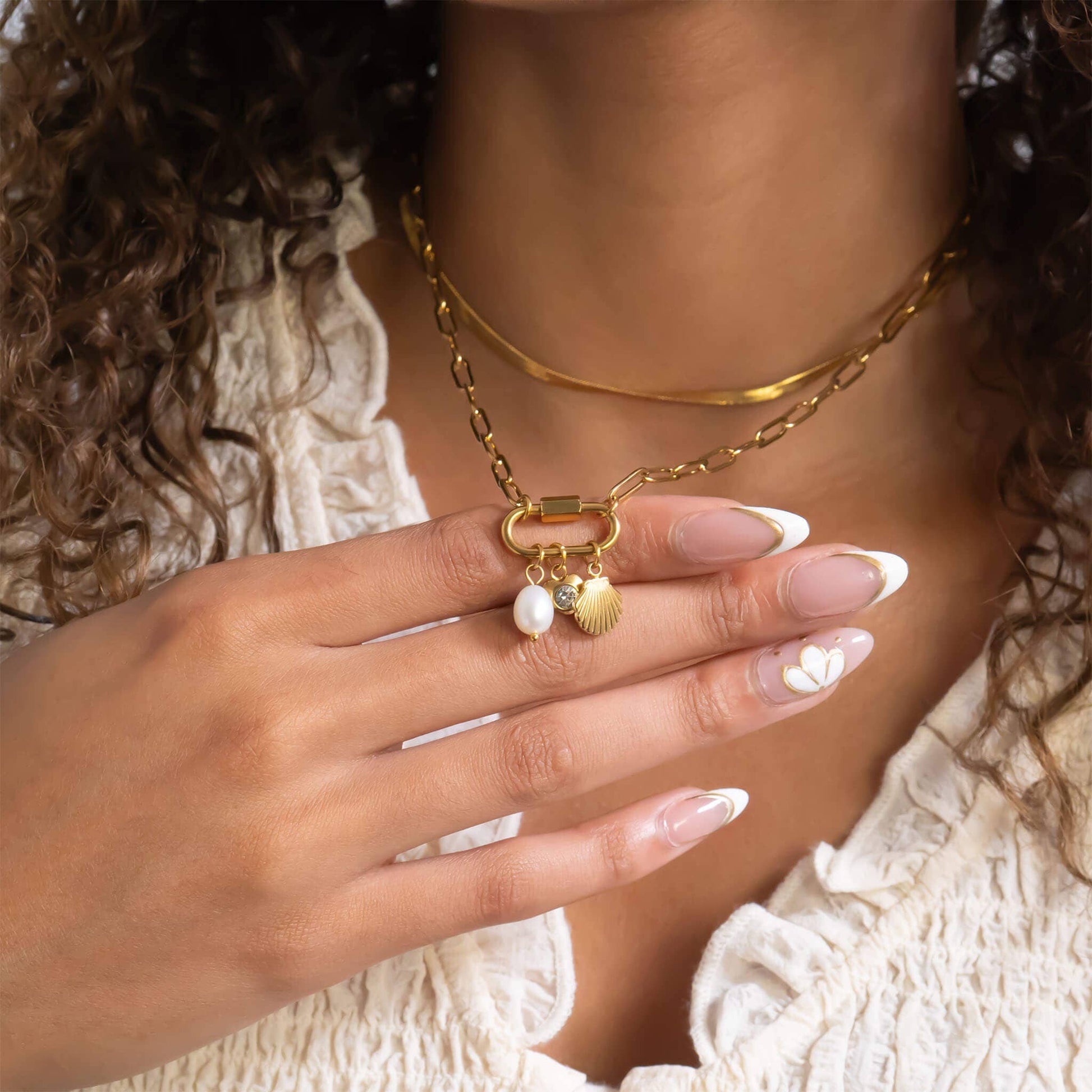 Close-up of a hand wearing a gold necklace with a pendant, set against a neutral background.
