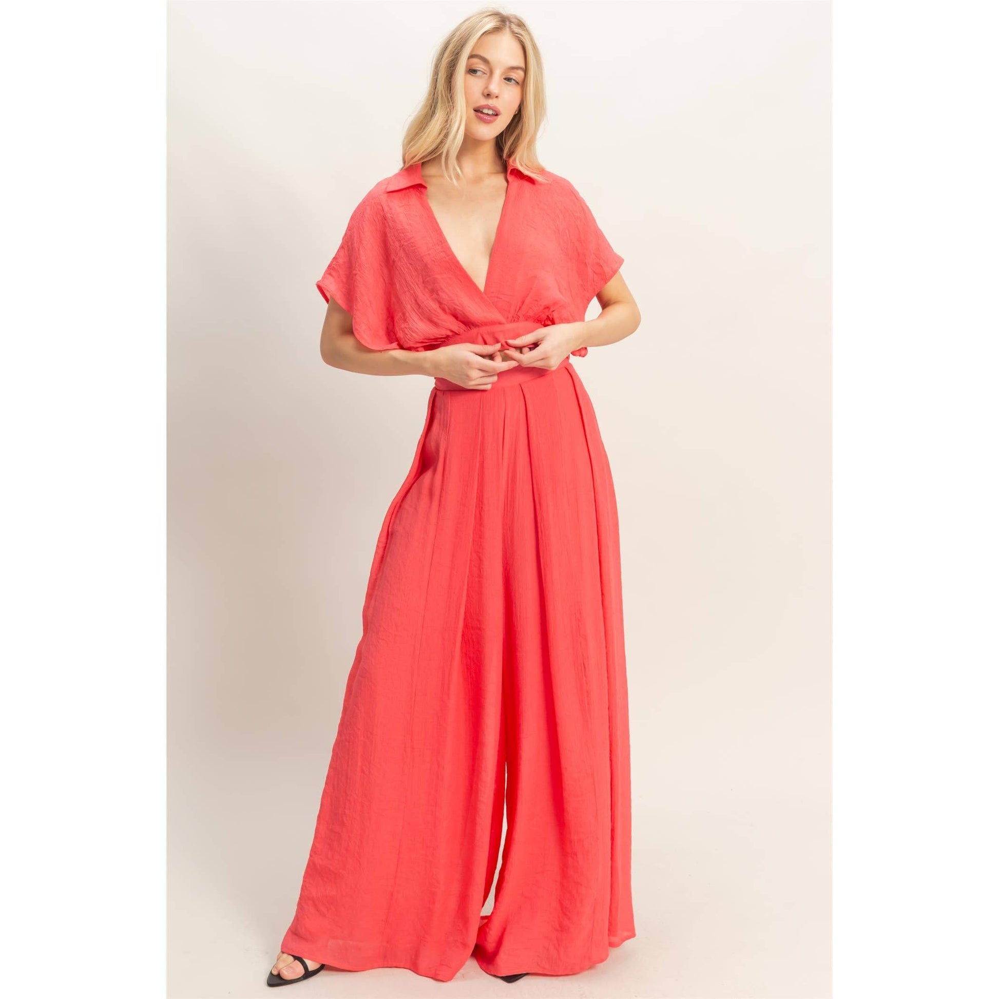Woman wearing a coral jumpsuit on a plain background
