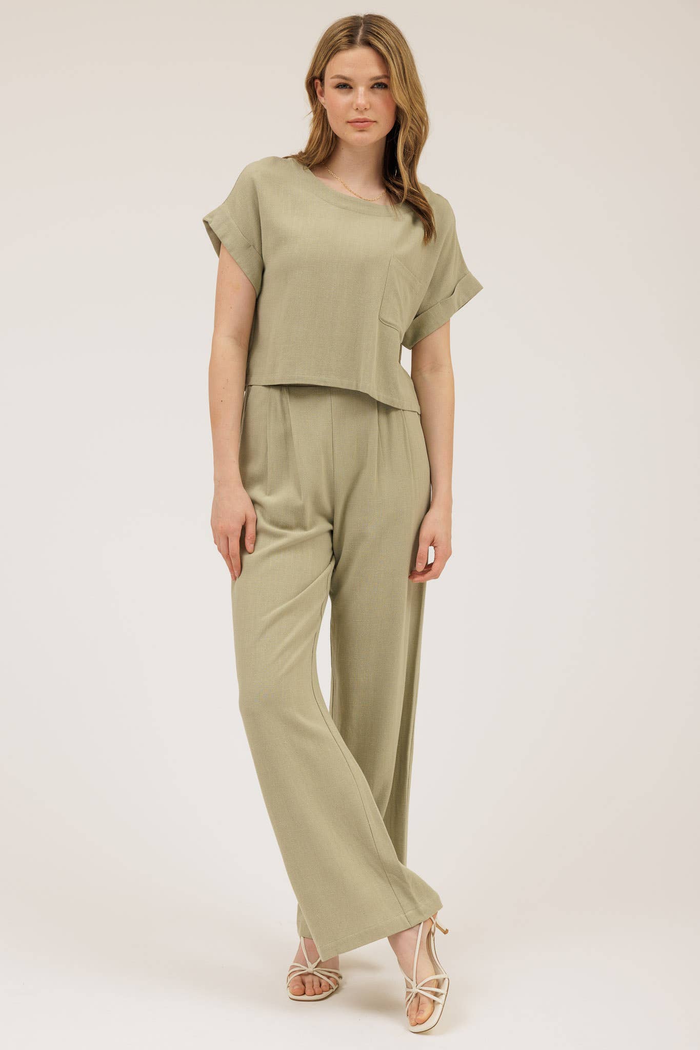 Woman wearing a matching olive green top and pants set on a white background