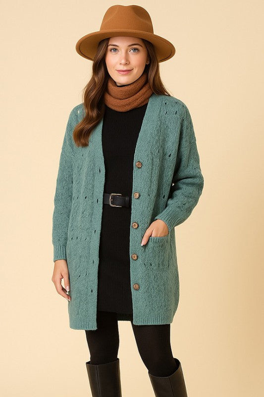 Woman wearing a teal cardigan, black dress, brown hat, and black boots on a beige background