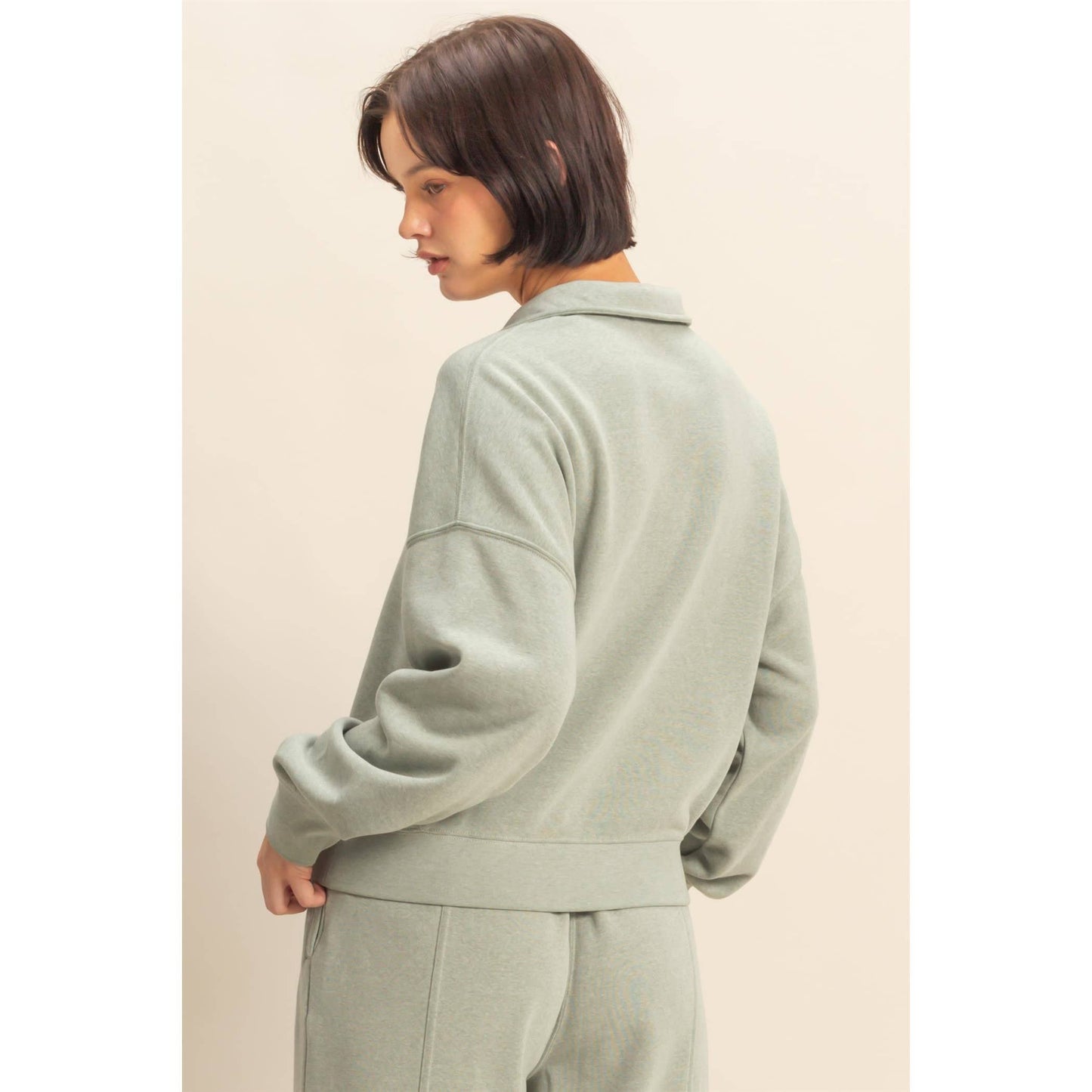 Person wearing a light green tracksuit against a beige background
