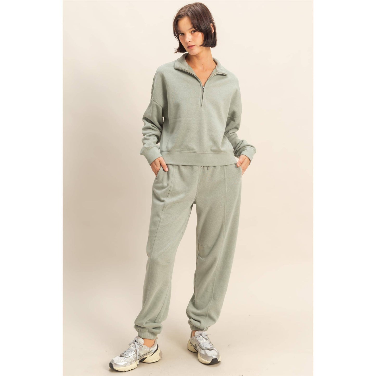 Woman wearing a light gray tracksuit with silver sneakers on a beige background