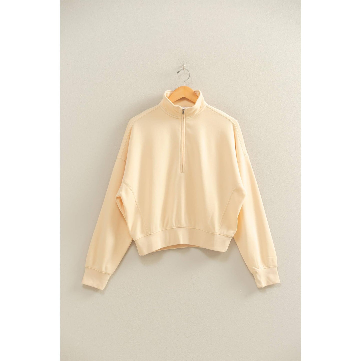Beige sweatshirt on a hanger against a plain background