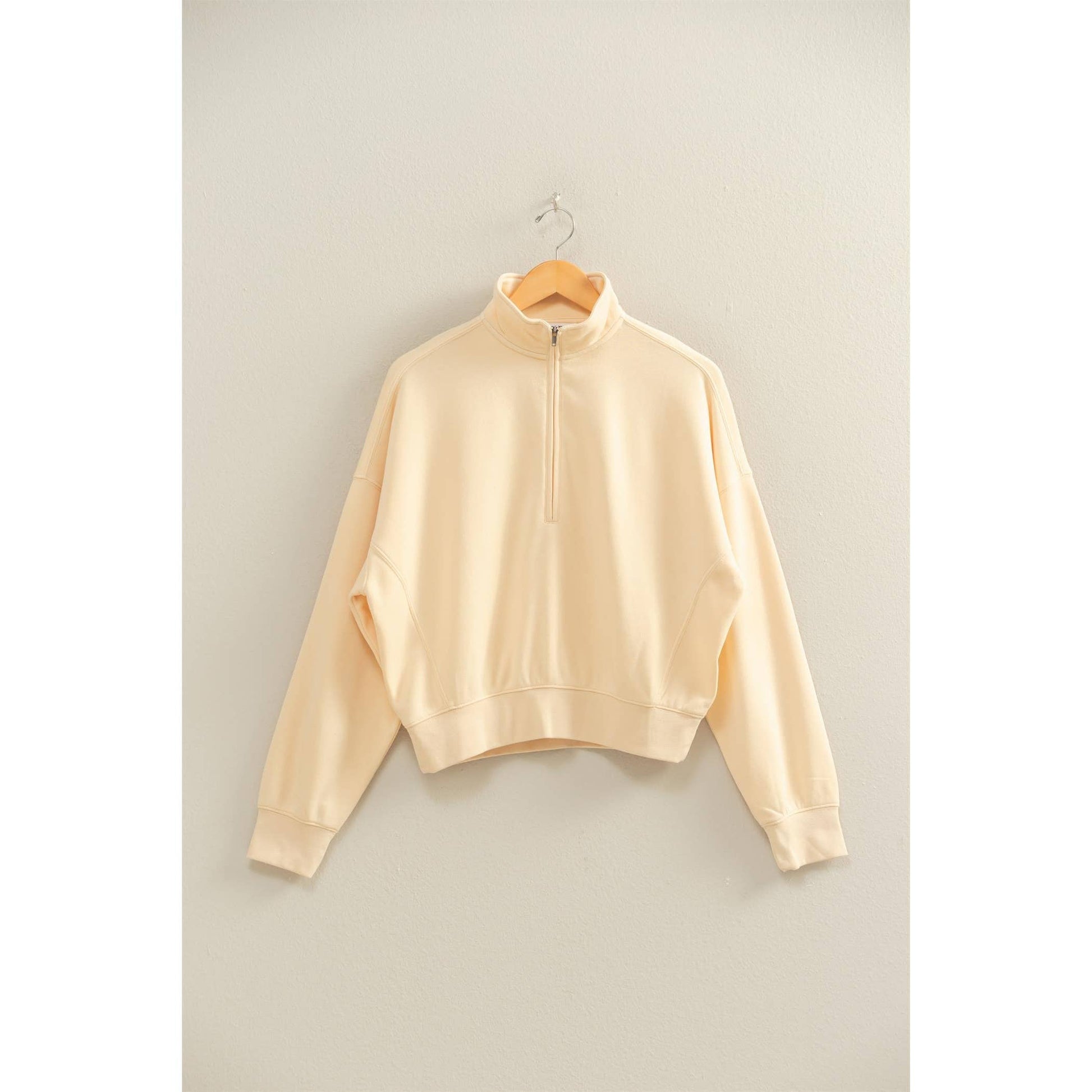 Beige sweatshirt on a hanger against a plain background