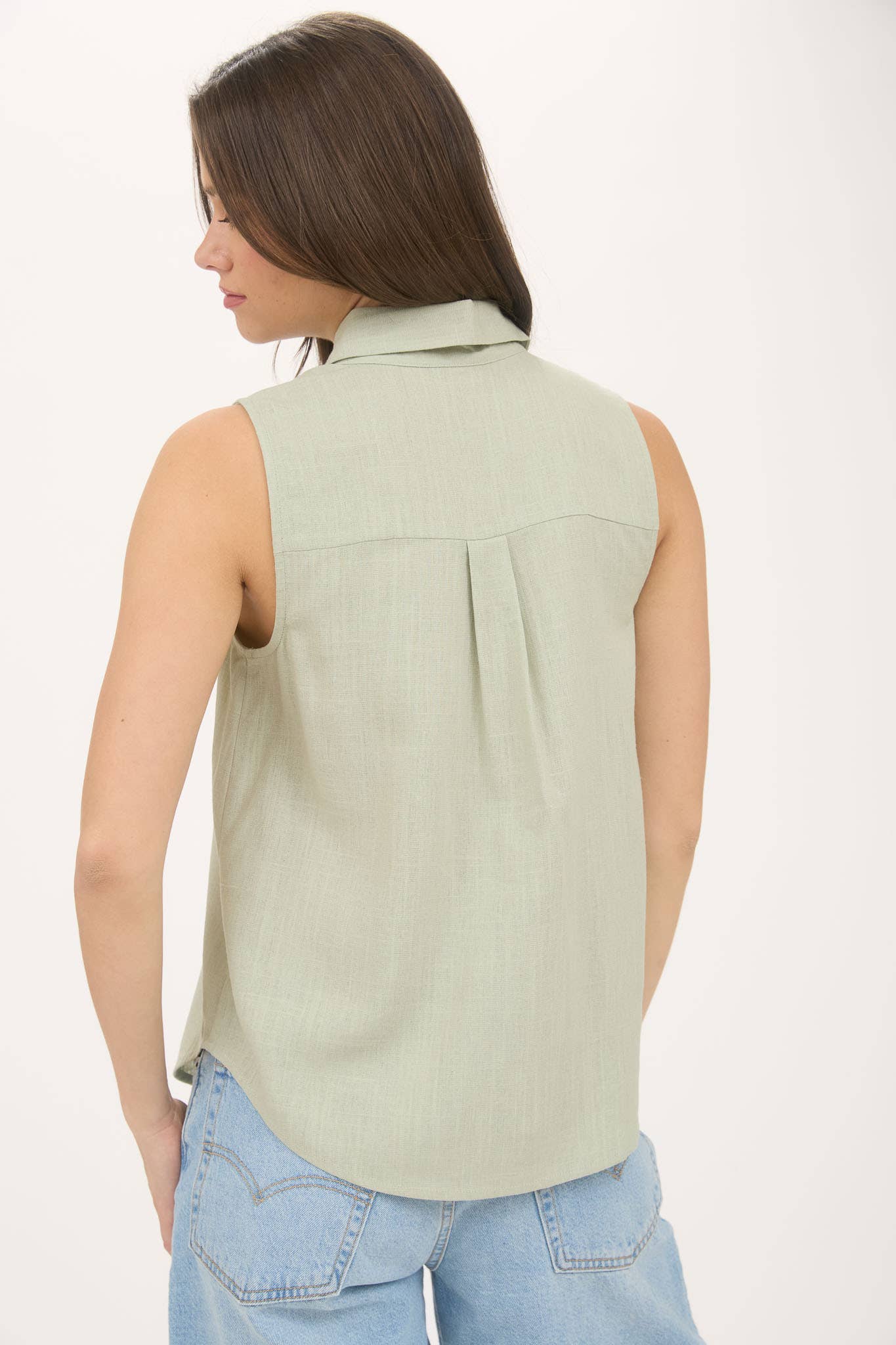 Woman wearing a light green sleeveless top and blue jeans on a white background