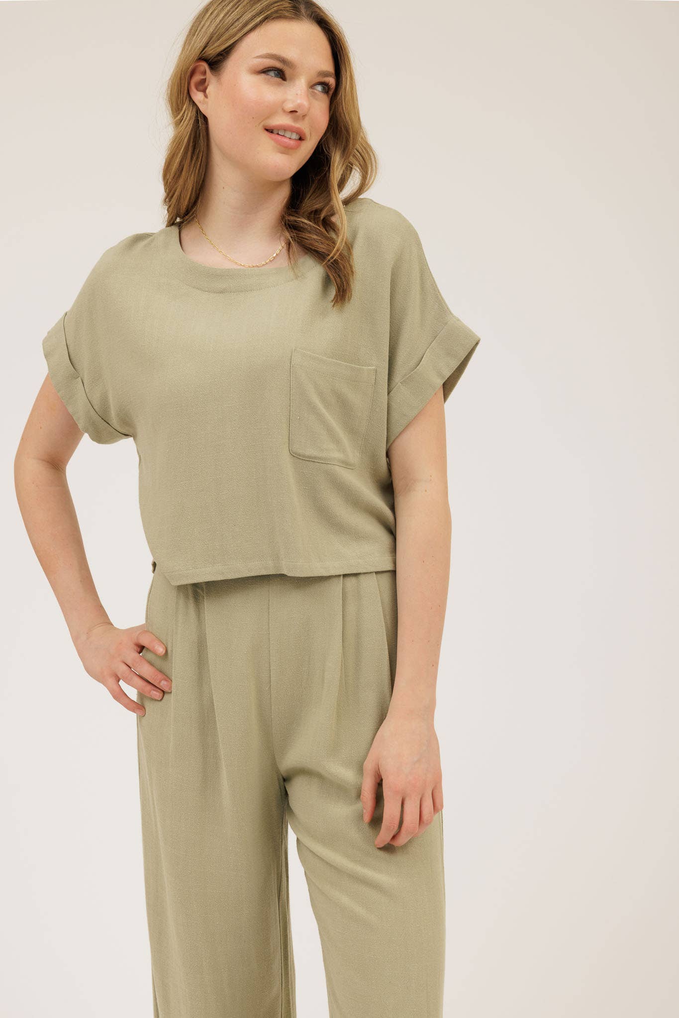 Woman wearing a matching olive green top and pants set on a plain background