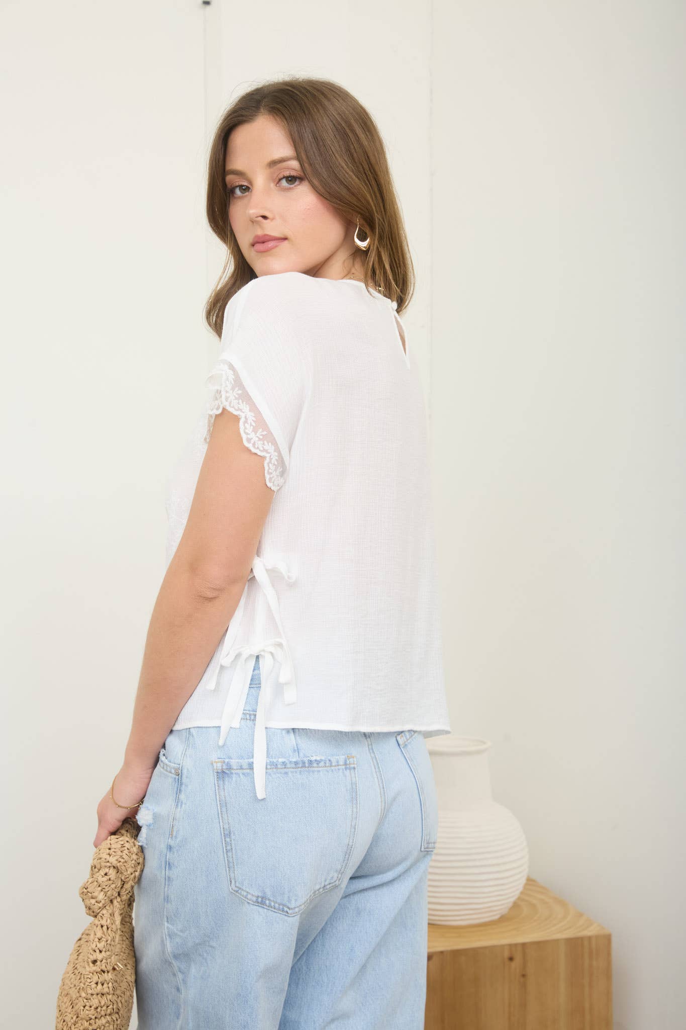 Woman wearing a white blouse and light blue jeans against a plain background