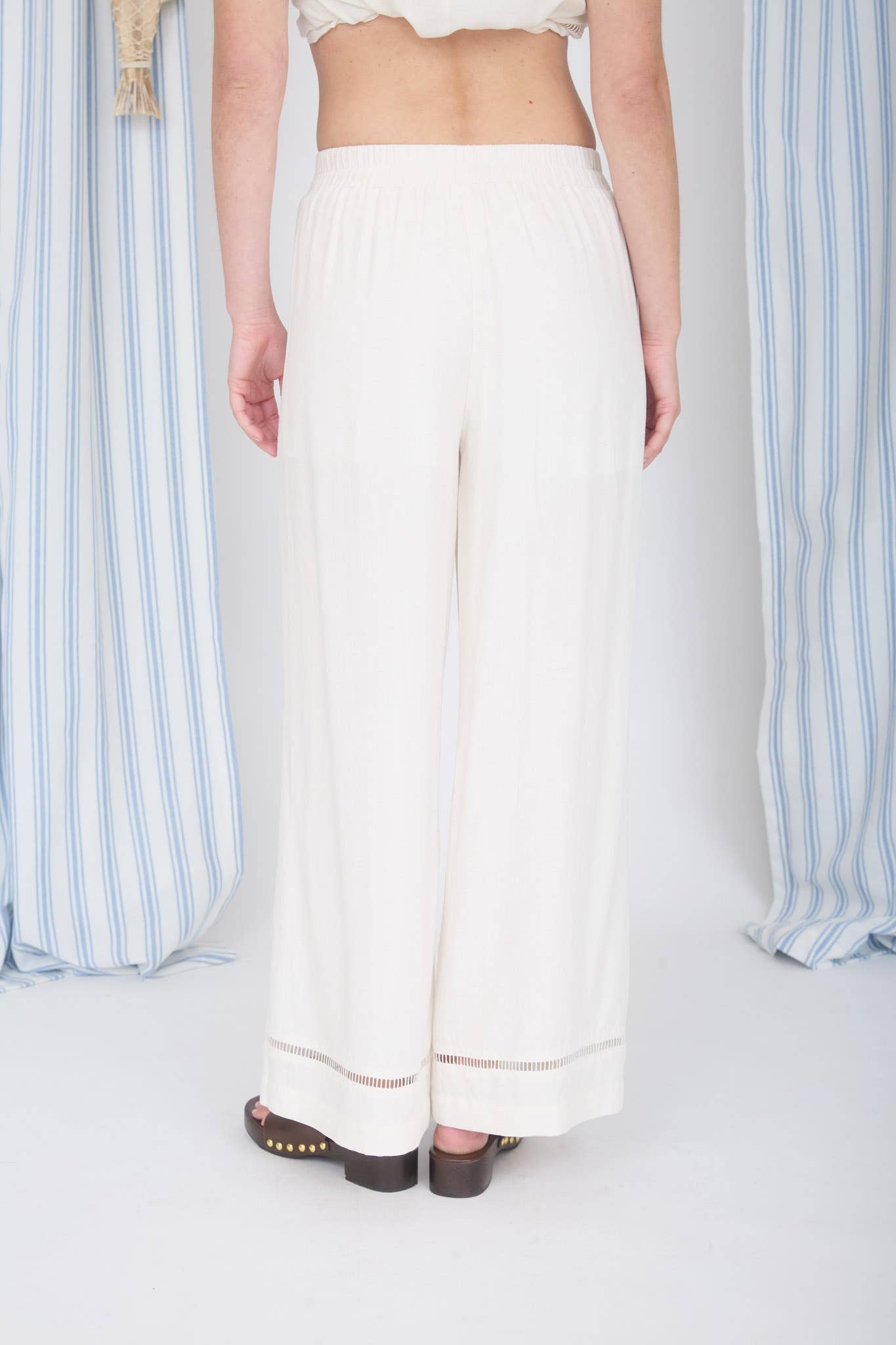 Person wearing white pants with a striped curtain background