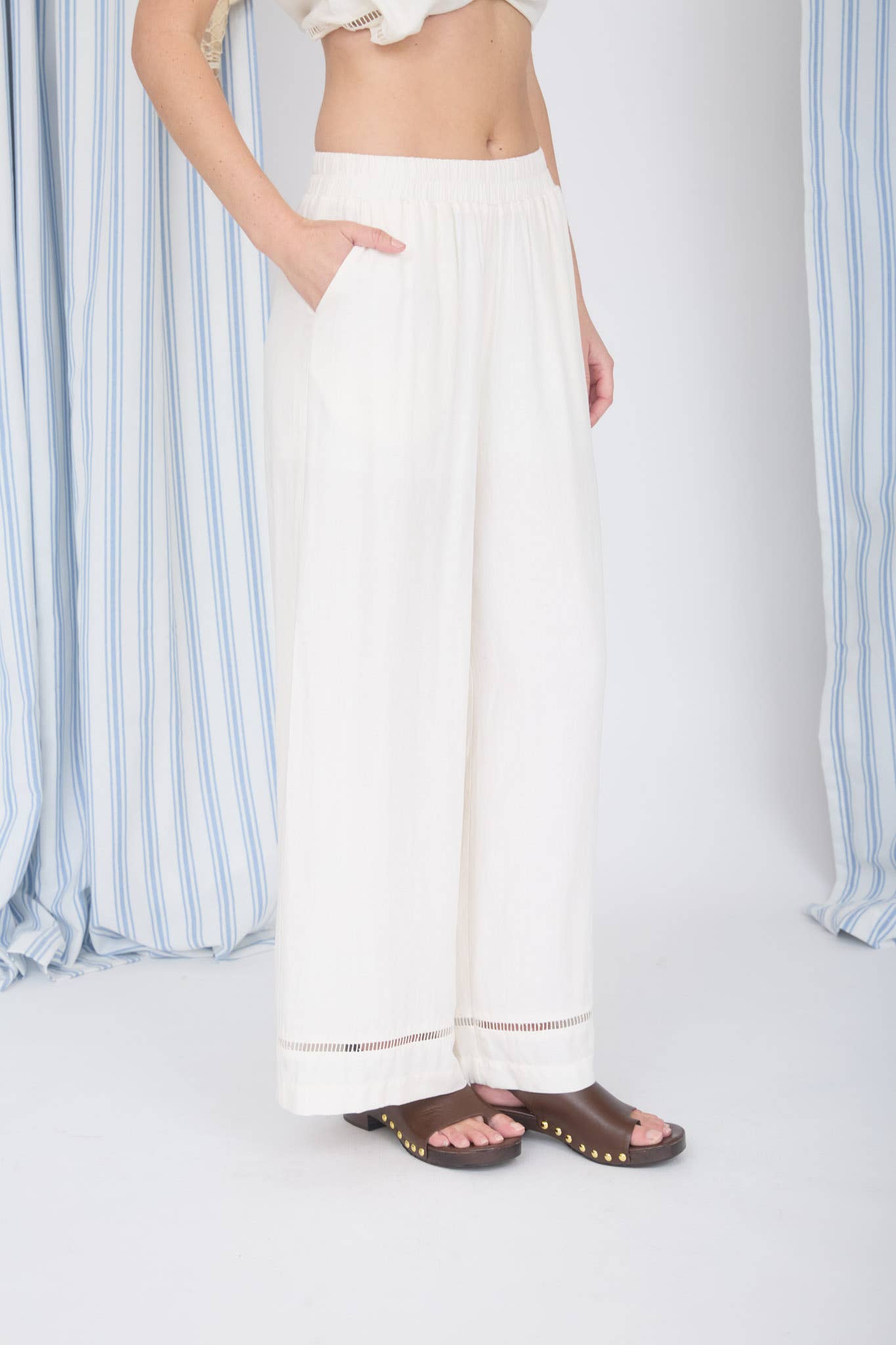 Person wearing white pants with a striped curtain background