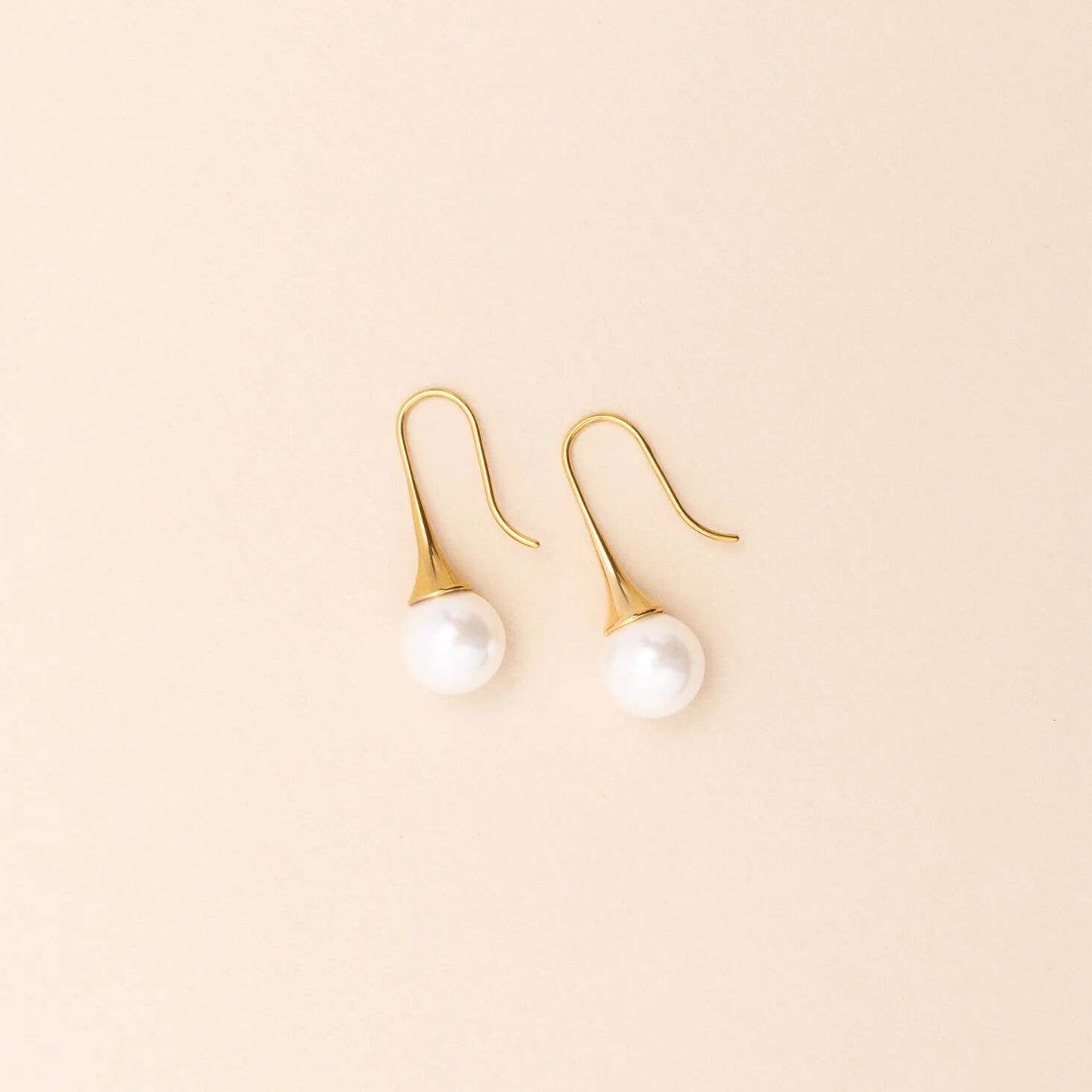 Gold earrings with pearl drops on a beige background