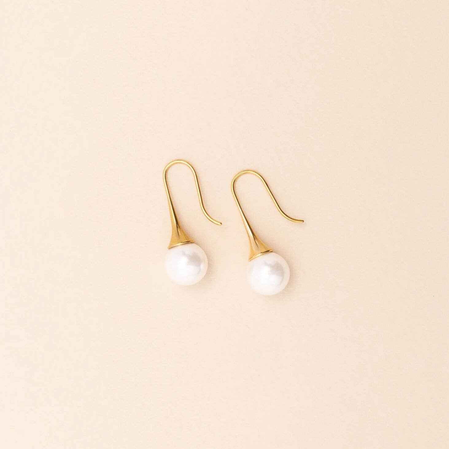 Gold earrings with pearl drops on a beige background
