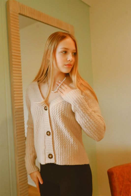 Woman wearing a beige cardigan in front of a mirror