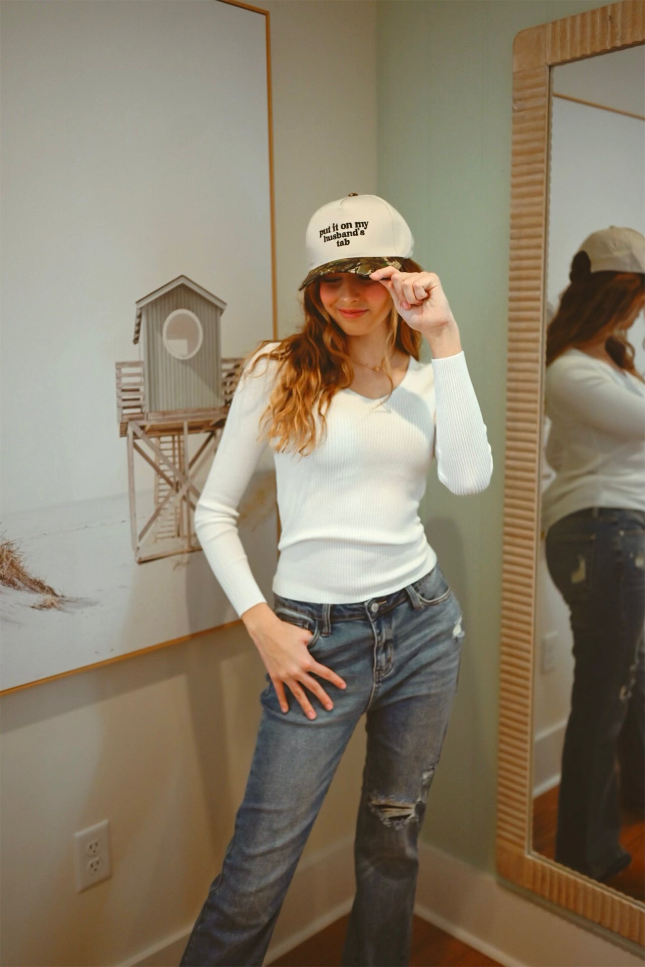 Person wearing a white cap and long-sleeve shirt in front of a mirror.