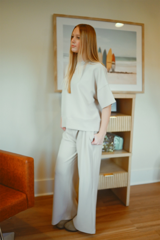 Woman in a light beige outfit standing in a room with a framed picture on the wall.