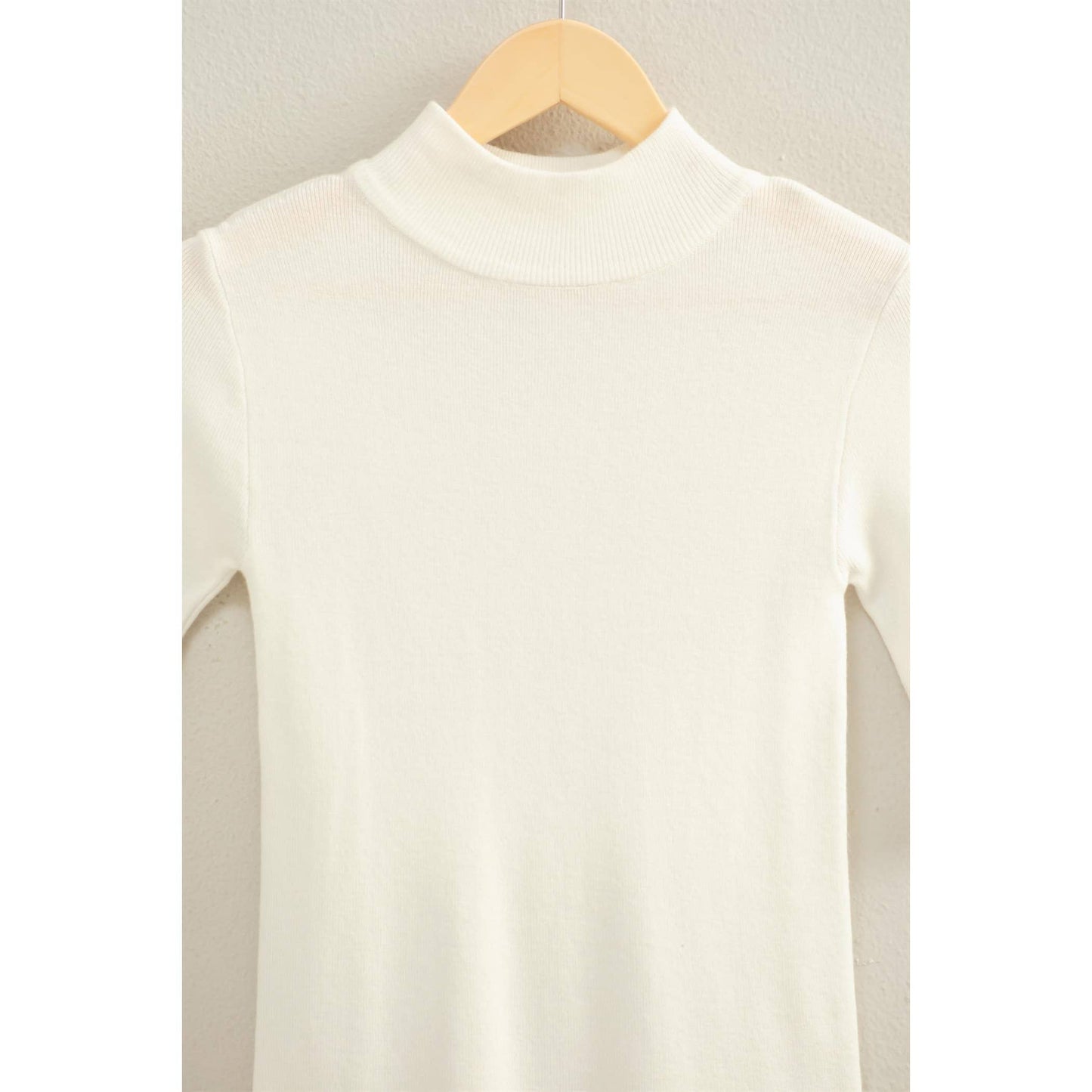 White three-quarter length sleeve top on a wooden hanger against a light background