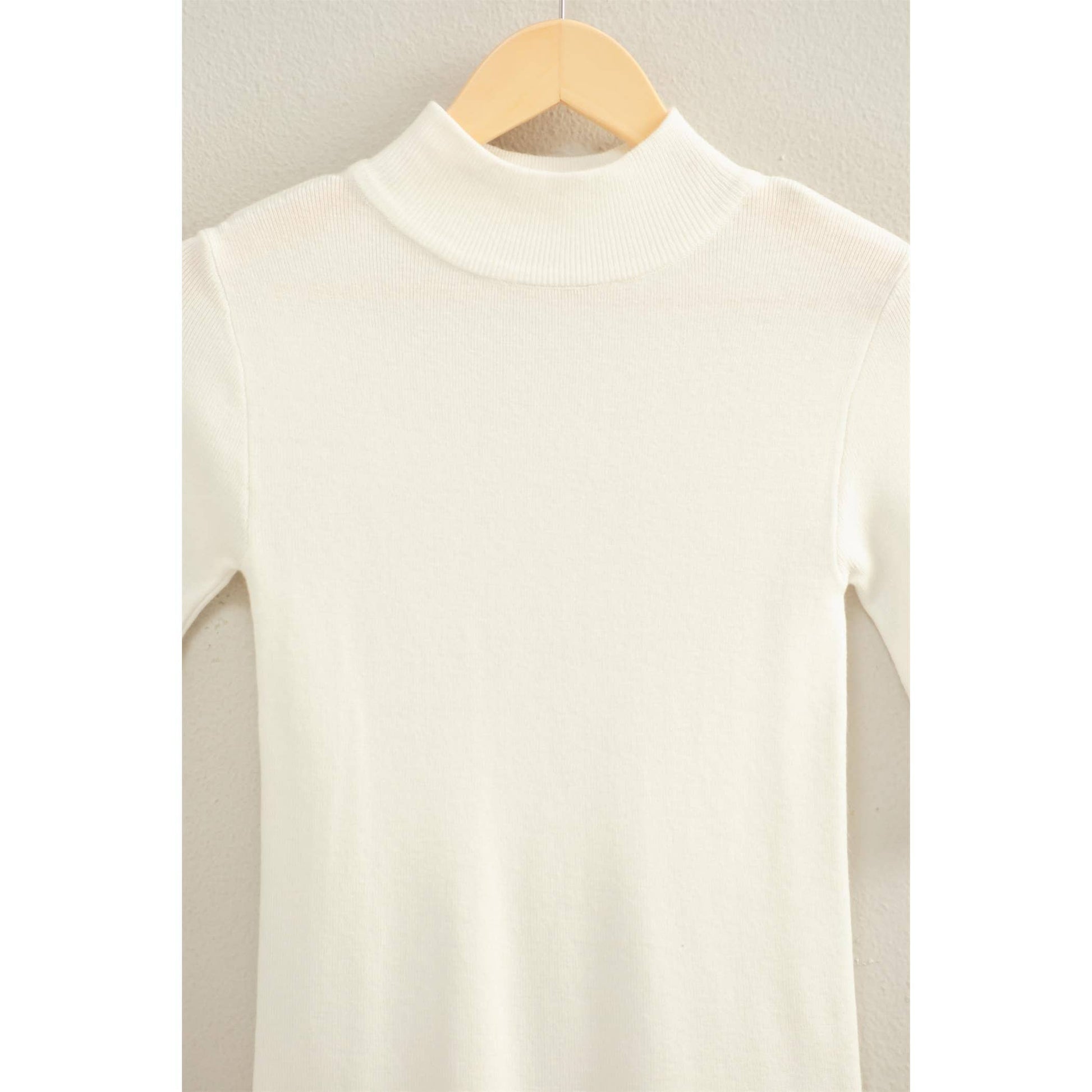 White three-quarter length sleeve top on a wooden hanger against a light background