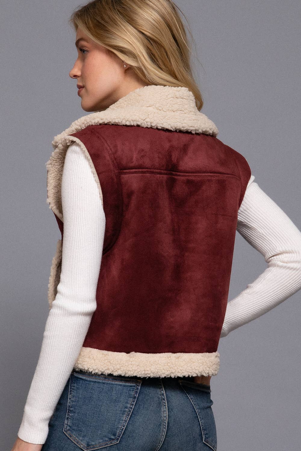 Person wearing a burgundy suede vest with beige interior on a gray background