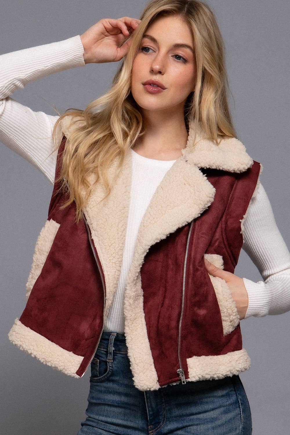 Woman wearing a burgundy suede vest with white fur lining against a gray background