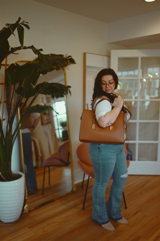 Woman holding a brown handbag in a room with a large mirror and plant.